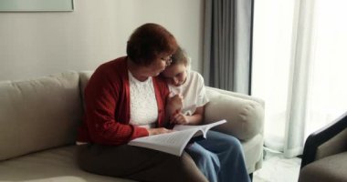 Mutlu aile ilişkileri. Birlikte masal okumaktan zevk alıyoruz. Sevimli kızıl saçlı küçük kız gülümsüyor ve sevgi dolu büyükannesiyle hafta sonunu evde geçirdiğini söylüyor. 4K 'da yavaş çekim