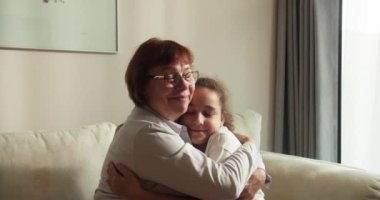 Sevgi dolu yaşlı büyükannenin yanaklarından öptüğü küçük 10 'lu yaşlarda bir torun, aile kanepeye oturur şefkat dolu bir anın tadını çıkarır, sevgi ve şefkat gösterir, bağlılık ve samimi duygular ifade eder.
