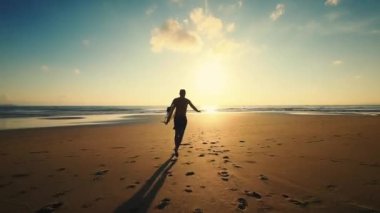 Turuncu yaz günbatımı. Macera ruhu, başarı, doğa. İnce erkek sörfçü kumsalda kumsalda uzun bir sörf tahtası alır ve ılık okyanus suyu boyunca koşar. 4K