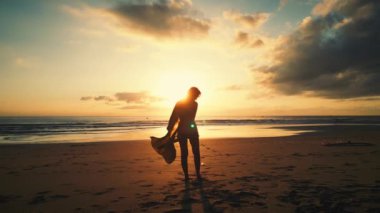 Deniz kenarında güzel bir gün batımı. Deniz kenarında, turuncu bir günbatımında dalgalar boyunca güneşe doğru koşan bir kadın, turuncu bir yaz günbatımında ılık okyanus suyunda yürüyen bir kız. 4K 'da yavaş çekim.