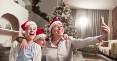 Torunu ve torunuyla birlikte Noel 'de Noel ağacının önünde telefonuyla selfie çekiyorlar. Noel sabahı mutlu anlar Mutlu çocuk ve büyükanne.