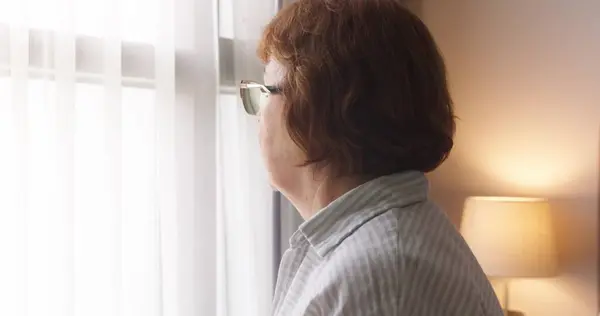 Kafkasyalı yaşlı bir kadın rahat bir yatak odasında yatağında sırt ağrısı çekiyor. Rahatlamak için sırtını iki eliyle tutuyor.