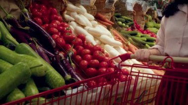 Güzel, genç, esmer, güzel bir kadın marketten yiyecek, domates alıyor. Kız ürünleri, sebzeleri, meyveleri dükkandan seçiyor. Alışveriş, vegan satış konsepti. 4K