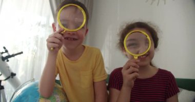 Çocuk aktiviteleri. Neşeli ve tatlı bir gülümseme, elinde büyüteç, oyun, kahkaha ve kameraya bakan, gün batımının altında ev ortamında oturan neşeli bir kız ve oğlan
