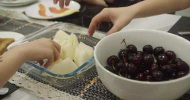 Çocukların elleri beyaz bir tabaktan kırmızı bordo kirazları yerken kırmızı kirazları alıyor. 4K