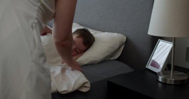 Anne oğluna bakıyor. Yatakta uyuyan bebek. Yan yatmış uyuyan çocukla yüzleş. İzleme, gece yarısı uyuyan bebeği vurdu. Küçük erkek bebek beşiğinde tatlı tatlı uyuyor ve uykusunda gülümsüyor.