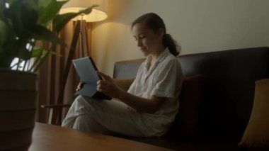 Çocuk tablette oyun oynuyor ya da kız bilgisayar öğreniyor heyecanlı ve eğlenceli çalışmayı internette öğreniyor. Akşamları evdeki oturma odasındaki kanepede oturan çocuk pijamalarıyla tableti kullanıyor.