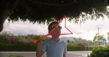 Joy Kid yaz günü sabun köpüğüyle oynuyor. Yeşil ağaçların arka planına sabun köpüğü üfleyen mutlu çocuk. Küçük çocuk doğada dinleniyor. Aile hafta sonu kavramı. Tatil sabun köpükleri