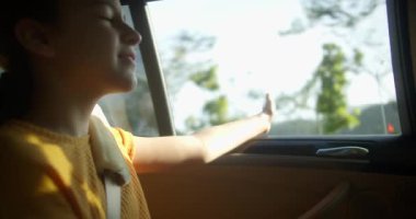 Gülümseyen kız rahatlıyor, seyahatin tadını çıkarıyor, seyahat hayali kuruyor, araba maceraları, çocuk hafta sonu tatili, tatil. Aile seyahati. Çocuk, rüzgar yolu gezisi için elini oynat. Yaz araba yolculuğu açık pencere.