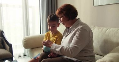 Çocuk, yakın planda kumbarada para biriktiriyor. Büyükannesi kumbaraya bozuk para atarken çocuk mavi kumbarasını elinde tutuyor. Çocuklar maddi olarak güvende. Finansal tasarruflar.