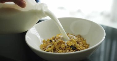 Sağlıklı kahvaltıda gevrek gevreğin içine süt dökülen bir kadın. Gevrek granola dolu beyaz bir kaseye yavaş yavaş süt dökülüyor..