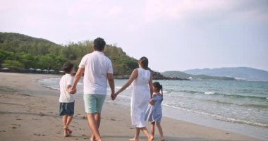 Asyalı genç mutlu aile akşamları sahilde tatilin tadını çıkarıyor. Baba, anne ve çocuklar gün batımında deniz kenarında yürürken rahatlar. Hayat tarzı seyahat tatil yaz tatili konsepti. 4K ağır çekim. 4K