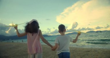 Kumsalda koşan oyuncak uçaklarla oynayan mutlu beyaz çocuklar. Küçük çocuklar, erkek ve kız kardeşler plajda koşuyorlar, oynuyorlar, aile tatili yapıyorlar. Küçük çocuklar için kumsal tatili kavramı. Oynayan çocuklar