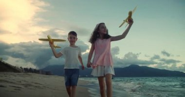 Kumsalda koşan oyuncak uçaklarla oynayan mutlu beyaz çocuklar. Küçük çocuklar, erkek ve kız kardeşler plajda koşuyorlar, oynuyorlar, aile tatili yapıyorlar. Küçük çocuklar için kumsal tatili kavramı. Oynayan çocuklar