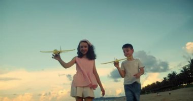 Kumsalda koşan oyuncak uçaklarla oynayan mutlu beyaz çocuklar. Küçük çocuklar, erkek ve kız kardeşler plajda koşuyorlar, oynuyorlar, aile tatili yapıyorlar. Küçük çocuklar için kumsal tatili kavramı. Oynayan çocuklar