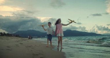 Kumsalda koşan oyuncak uçaklarla oynayan mutlu beyaz çocuklar. Küçük çocuklar, erkek ve kız kardeşler plajda koşuyorlar, oynuyorlar, aile tatili yapıyorlar. Küçük çocuklar için kumsal tatili kavramı. Oynayan çocuklar