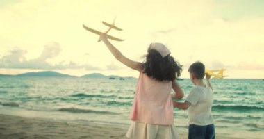 Kumsalda koşan oyuncak uçaklarla oynayan mutlu beyaz çocuklar. Küçük çocuklar, erkek ve kız kardeşler plajda koşuyorlar, oynuyorlar, aile tatili yapıyorlar. Küçük çocuklar için kumsal tatili kavramı. Oynayan çocuklar