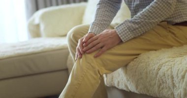 Erkek eller, evdeki oturma odasında kanepede otururken diz kaslarına masaj yapıyor.