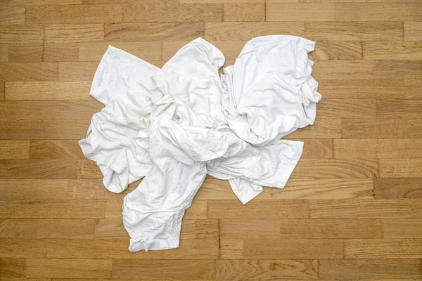 Messy dirty white sport t-shirts on wooden floor before washing in laundry