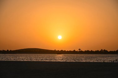 Çöl üzerinde gün batımı ve deniz ve palmiye ağaçlarının siluetleri ile Abu Dabi, arka plan olarak manzara