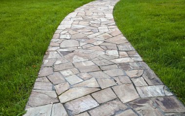 Bahçesinde yeşil çimenler olan taş kavis yolu.