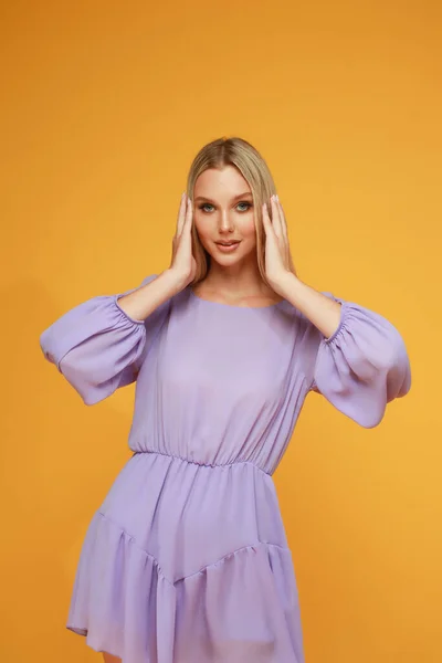 stock image Beautiful blonde girl in a lilac dress on a yellow background. Studio. Smile and emotions.