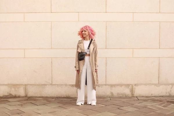 ピンクの髪をしたスタイリッシュな女の子のポートレート撮影 ベージュの色合い 春と夏の傾向2023 ベージュトレンチクローク白トップとパンツと 黒小さなベルトバッグ — ストック写真