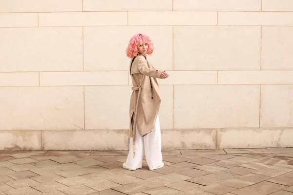 一个粉红头发的时髦女孩的肖像拍摄 米色阴影 2023年春季和夏季的流行趋势 米色海沟斗篷 白色上衣和裤子 黑色小皮包 — 图库照片