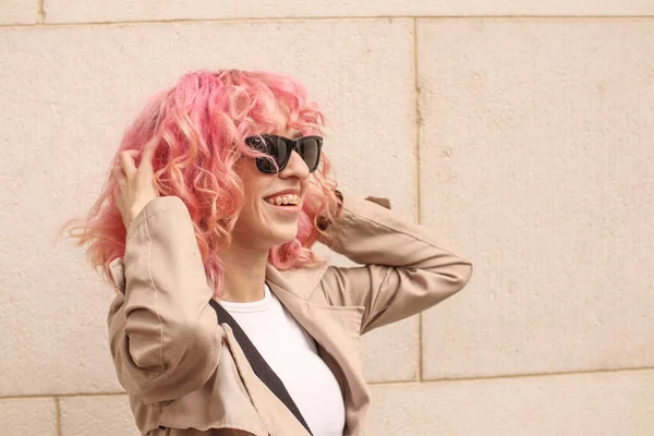 stock image Portrait shooting of a stylish girl with pink hair. Beige shades. Trends of spring and summer 2023.Beige Trench cloak with white top and pants. Black small belt bag