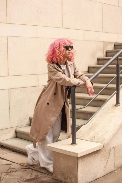 ピンクの髪をしたスタイリッシュな女の子のポートレート撮影 ベージュの色合い 春と夏の傾向2023 ベージュトレンチクローク白トップとパンツと 黒小さなベルトバッグ — ストック写真