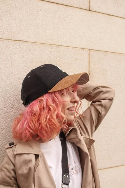 ピンクの髪をしたスタイリッシュな女の子のポートレート撮影 ベージュの色合い 春と夏の傾向2023 白のTシャツとベージュのパンツとベージュのトレンチコート 黒の小さなベルトバッグ ブラックキャップ — ストック写真