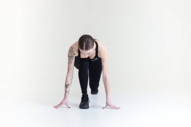 Kahverengi saçlı, siyah bluzlu ve beyaz arkaplanlı genç bir kız. Spor, spor, koşmaya başlar