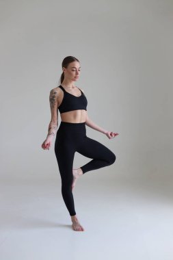 Kahverengi saçlı, siyah bluzlu ve beyaz arkaplanlı genç bir kız. Spor, spor, katlanmış kollarla durmak. Yoga