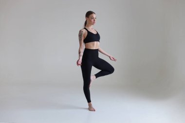 Kahverengi saçlı, siyah bluzlu ve beyaz arkaplanlı genç bir kız. Spor, spor, katlanmış kollarla durmak. Yoga