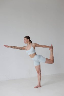 Kahverengi saçlı, gri bluzlu ve kulaklıklı beyaz arka planda şortu olan genç bir kız. Spor, spor, esneme ve yoga, meditasyon.