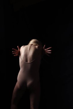 Bej bir elbise giymiş balerin. Karanlık arka plan. Güzel bir kadın vücudu. Bir jimnastikçi pozu.