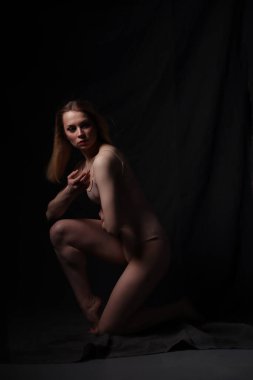 Bej bir elbise giymiş balerin. Karanlık arka plan. Güzel bir kadın vücudu. Bir jimnastikçi pozu.