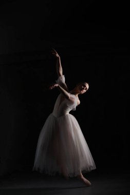 Profesyonel balerin dans ediyor. Beyaz elbiseli ve sivri uçlu ayakkabılı balerin. Karanlık arka plan. Güzel kadın vücudu..
