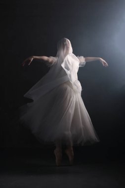 Profesyonel balerin dans ediyor. Beyaz elbiseli ve sivri uçlu ayakkabılı balerin. Karanlık arka plan. Peçe. Sahne. Performans