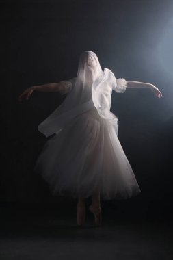 Profesyonel balerin dans ediyor. Beyaz elbiseli ve sivri uçlu ayakkabılı balerin. Karanlık arka plan. Peçe. Sahne. Performans
