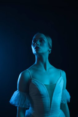 Profesyonel balerin dans ediyor. Beyaz elbiseli ve sivri uçlu ayakkabılı balerin. Koyu arkaplan, mavi ışık. Peçe. Sahne. Performans