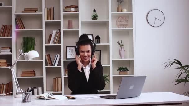 お気に入りのエネルギッシュディスコミュージックやダンスを聞くヘッドフォンを着てオフィスのラップトップコンピュータで働くラテン系ビジネス女性をハッピーリラックス フリーランスガール リラックス 休憩を取る — ストック動画