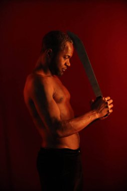 Koyu kırmızı arka planda çıplak bir vücudu ve palası olan zeki siyahi bir adamın portresi. Ninja, savaşçı, saldırganlık silueti