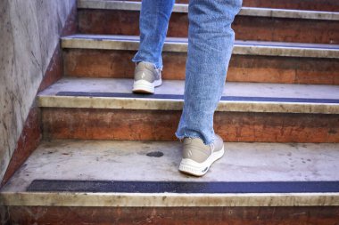Gündelik ayakkabılı genç bir kızın alt kısmı açık havada renkli merdivenlerde yürüyor, gençlik tarzı başarılı bir konsept.