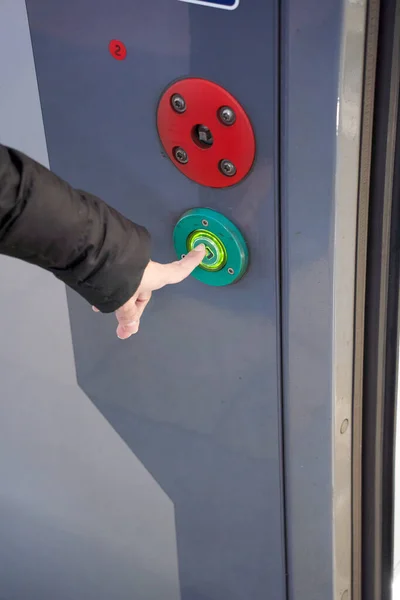 Button for opening doors on the train. Close-up of female hands on the green automatic door opener button
