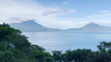 Guatemala 'daki Atitlan Gölü üzerinde yükselen ve arka planda volkanlar bulunan 4K video görüntüsü 