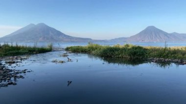 Gün doğumunda Atitlan Gölü Guatemala Gölü 'nde çekilen video görüntüleri. Arka planda volkanlar ve nehre saldıran kuş sürüleri var.