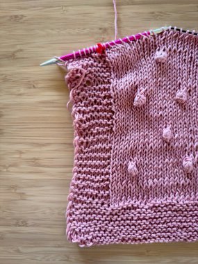 Ahşap arka planda pembe yün örgü iğneleri.