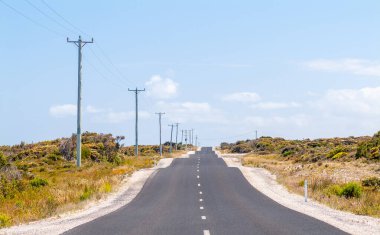 Ağır dalgalı ve engebeli bir yol, Tazmanya, Avustralya 'da yaz aylarında gökyüzünün altında elektrik hatları ve ısı pusuyla uzanıyor.