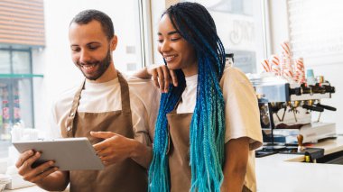 Kahve dükkanında bayan meslektaşımla çalışan mutlu bir adam. Barista ekrana ve yazıya bakarken tablet kullanıyor. Çevrimiçi düzen